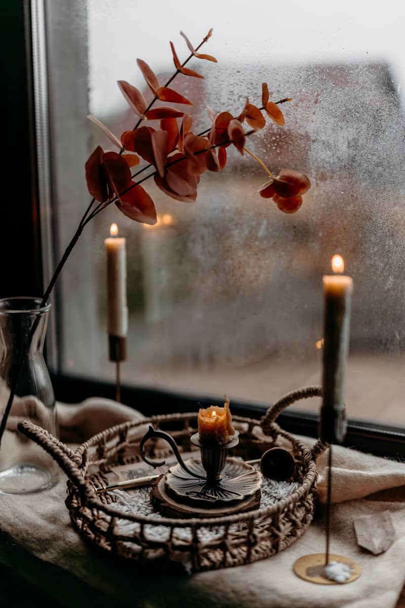 Candles and eucalyptus branch by a rainy window.
