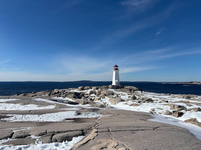 White lighthouse on rocky shore with snow.