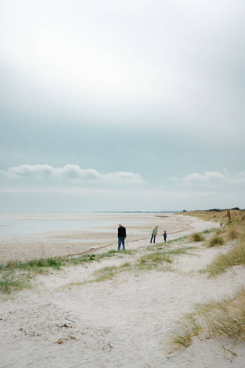 People walking on a sandy beach under a cloudy sky.