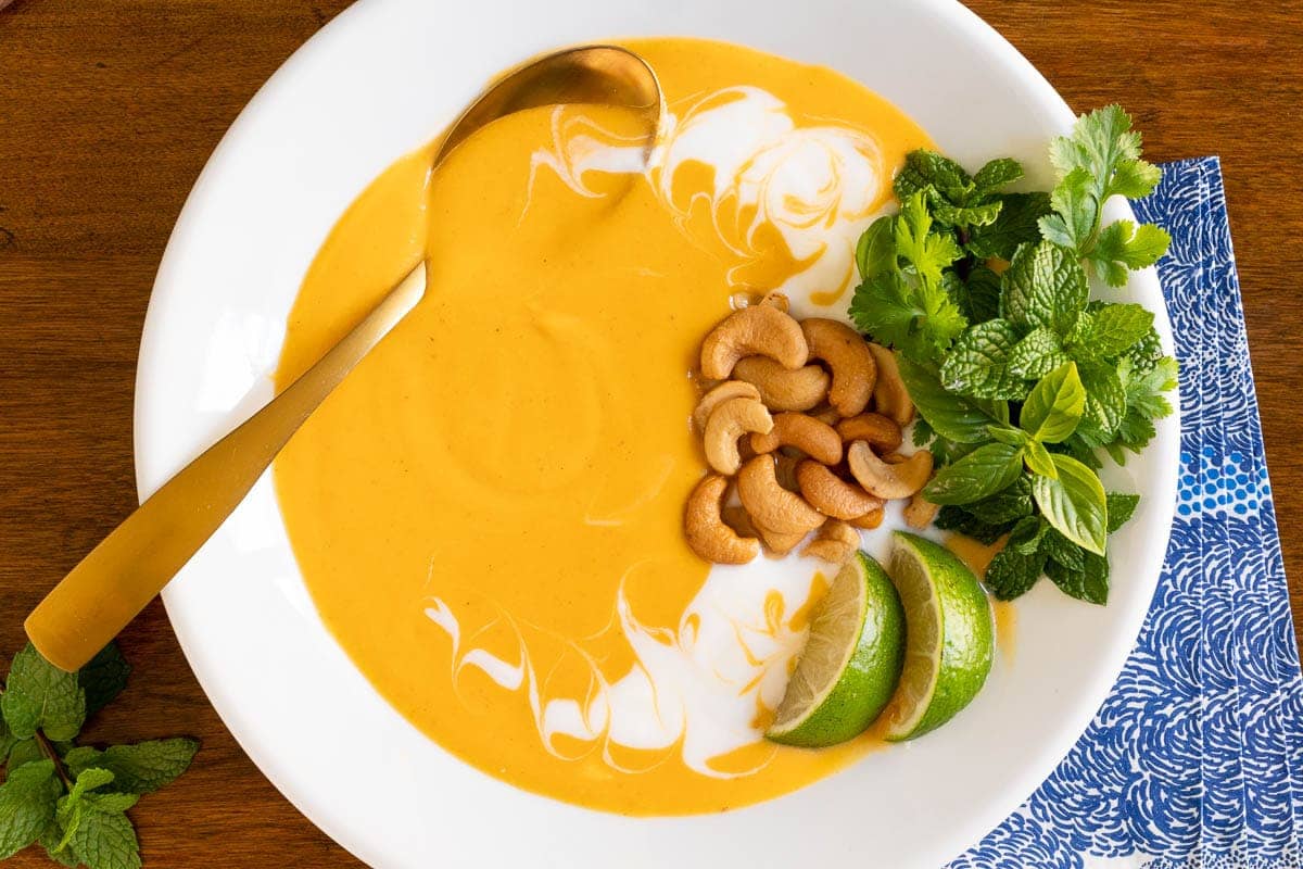 Roasted butternut squash soup with yogurt, cashews, herbs and lime in a white bowl.