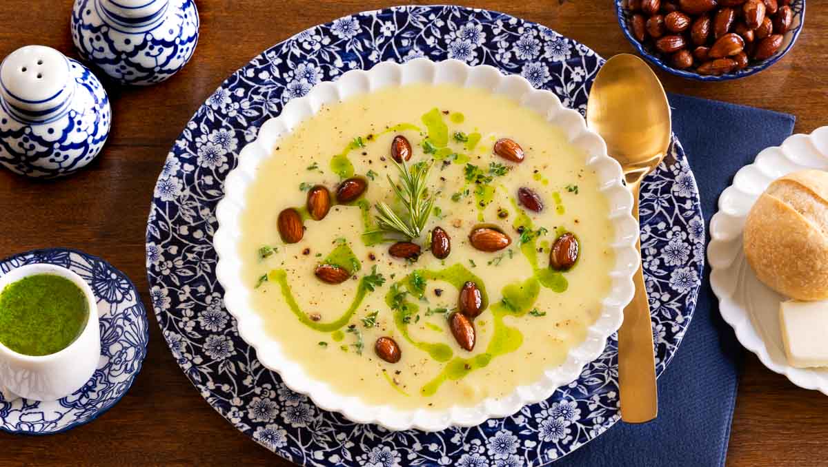 Creamy Cauliflower soup in a white scalloped bowl with fresh herb oil, and almonds