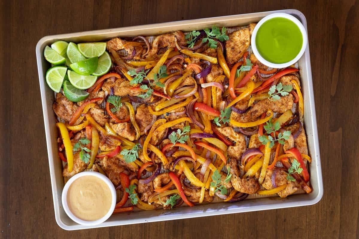a batch of easy sheet pan fajitas complete with lime wedges and dipping sauces