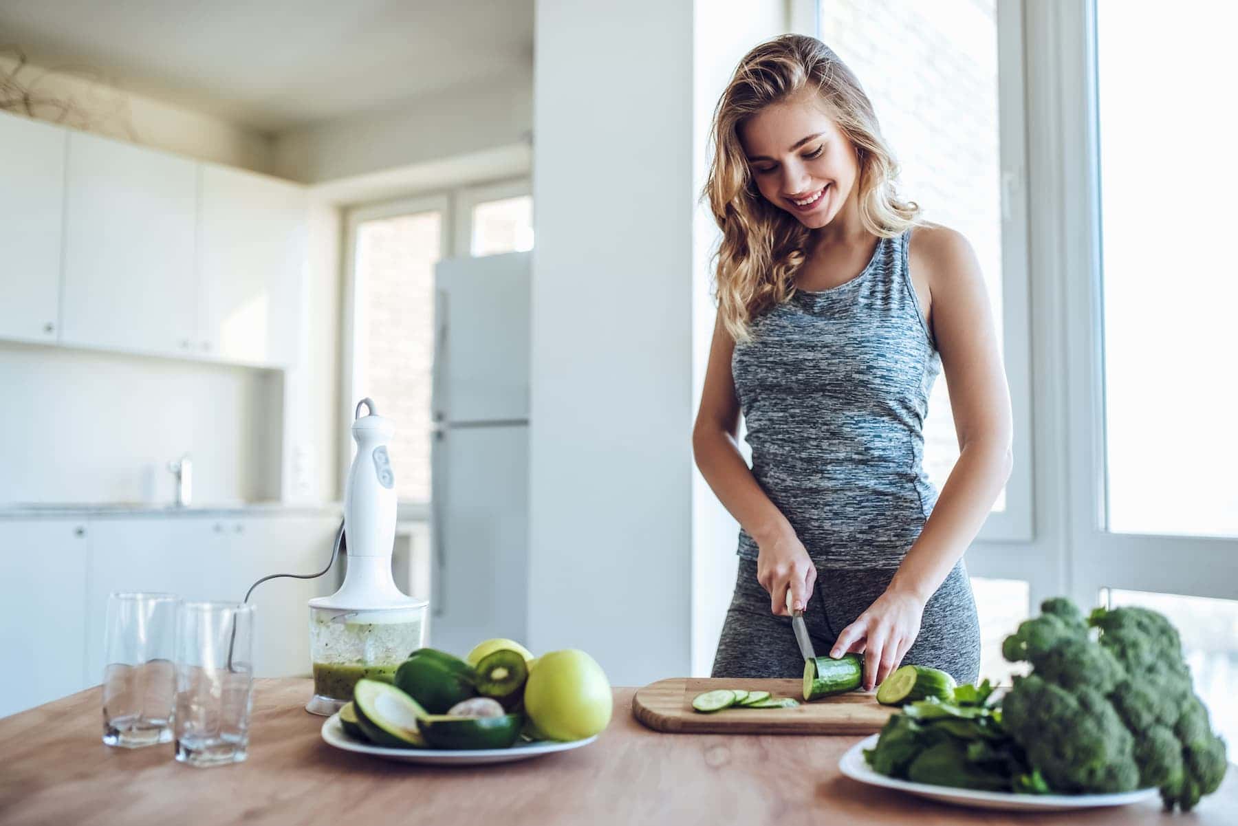 A woman cuts cucumbers in her kitchen after a workout, following her daily routine for a healthy lifestyle.
