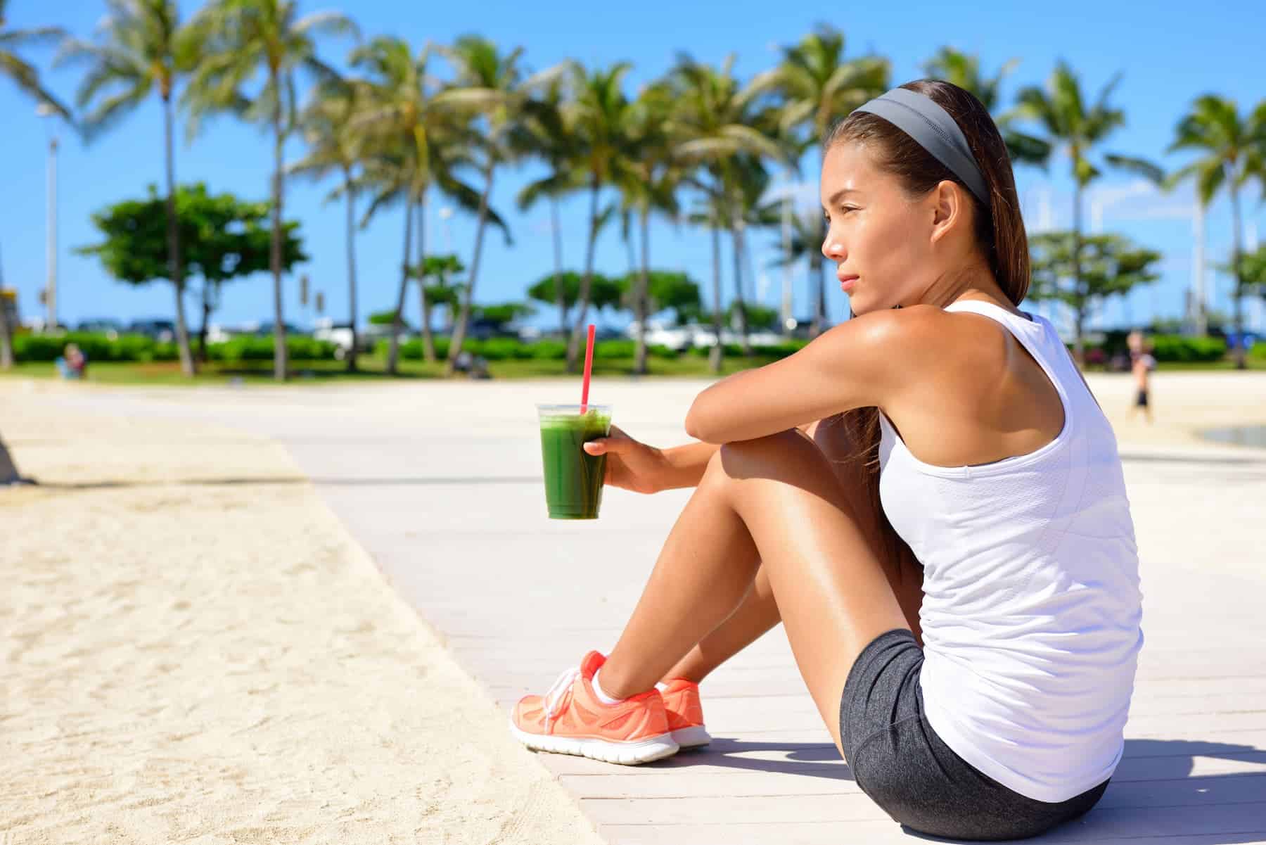 Runner woman drinking green smoothie resting and relaxing after running unaware that smoothies may not be good for weight loss.