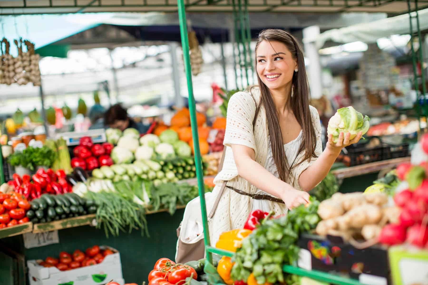 Young woman at a market choosing fresh fruits and vegetables, illustrating the Mediterranean Diet Pyramid lifestyle approach.