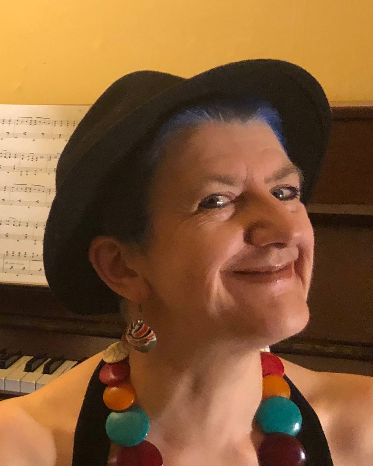 Close-up of Clare in a hat, grinning in front of a piano!