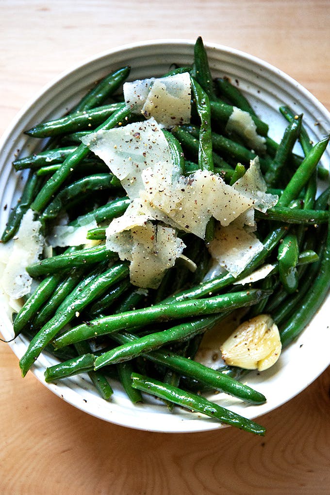 A skillet filled with cooked green beans topped with shaved parmesan. 
