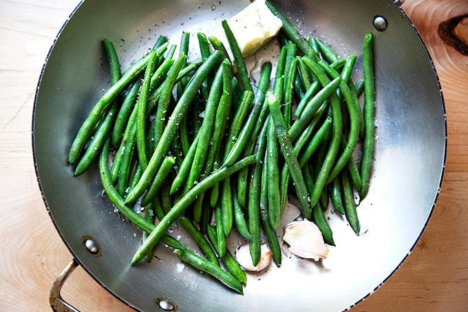 A skillet filled with green beans, butter, garlic, and water. 