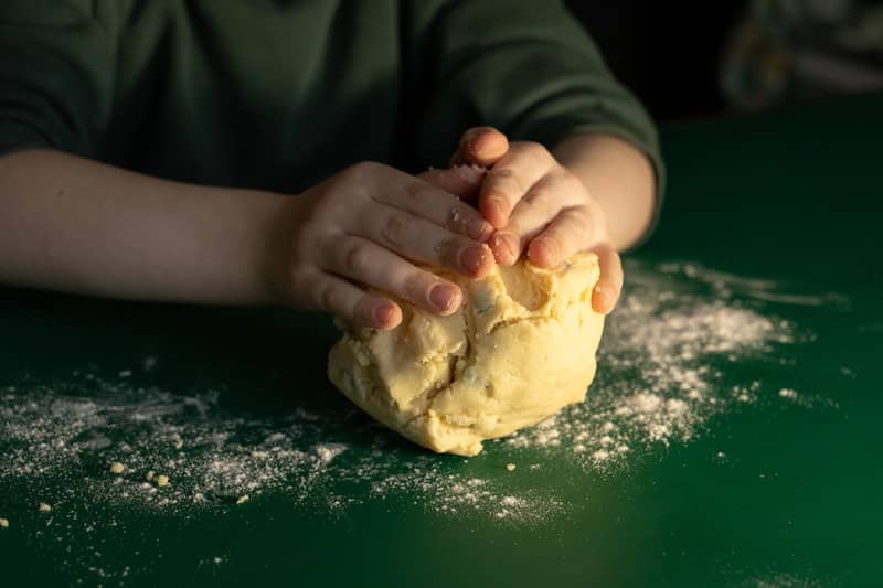 Child's hands kneading dough on a green surface.