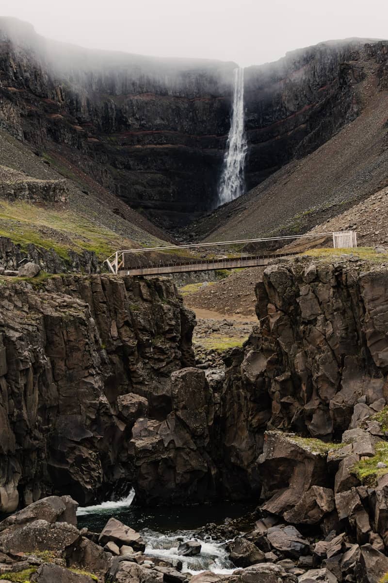 Tall waterfall cascading down a rocky canyon under fog.