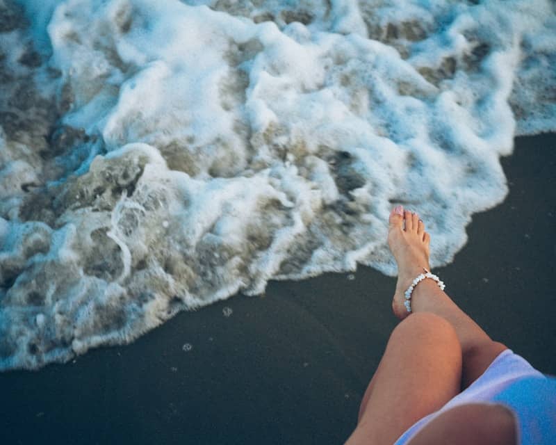 A person's legs and feet at the ocean's edge.