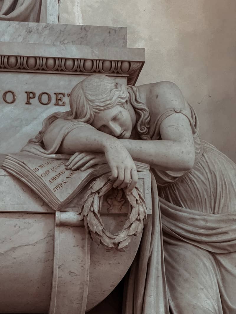 Marble sculpture of a grieving woman resting on a book.