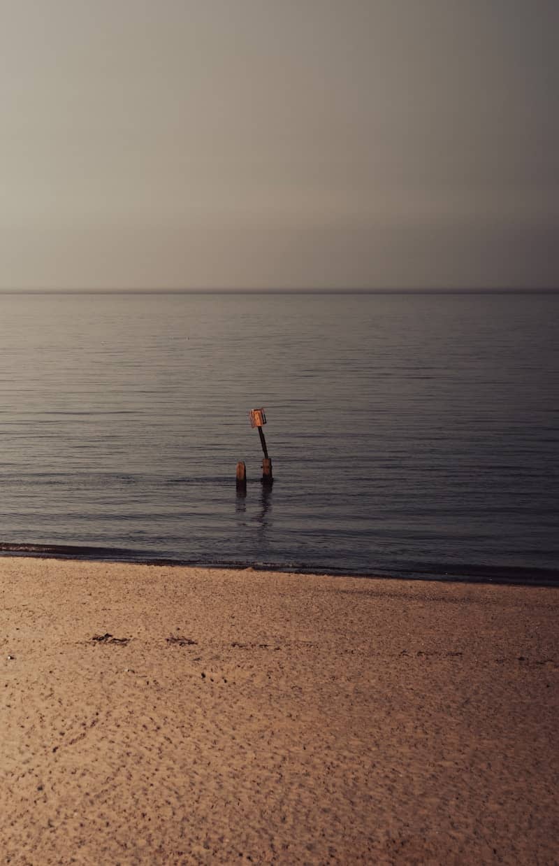 Calm beach with two posts and an orange marker.
