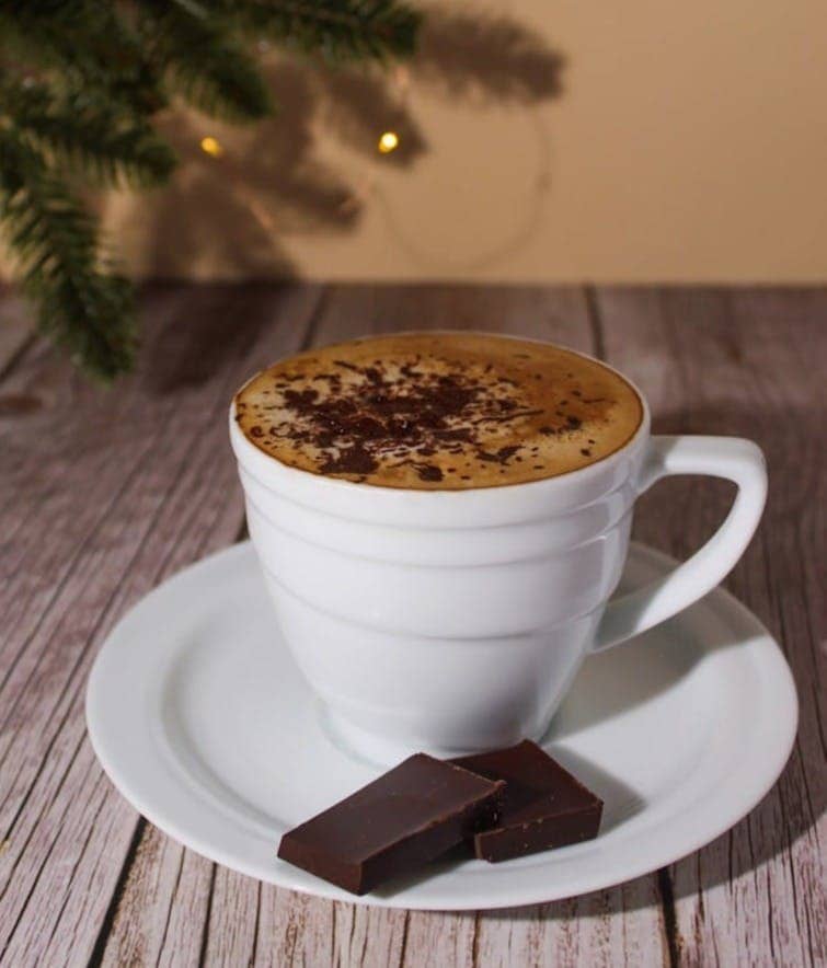 A cup of hot chocolate on a saucer next to a christmas tree