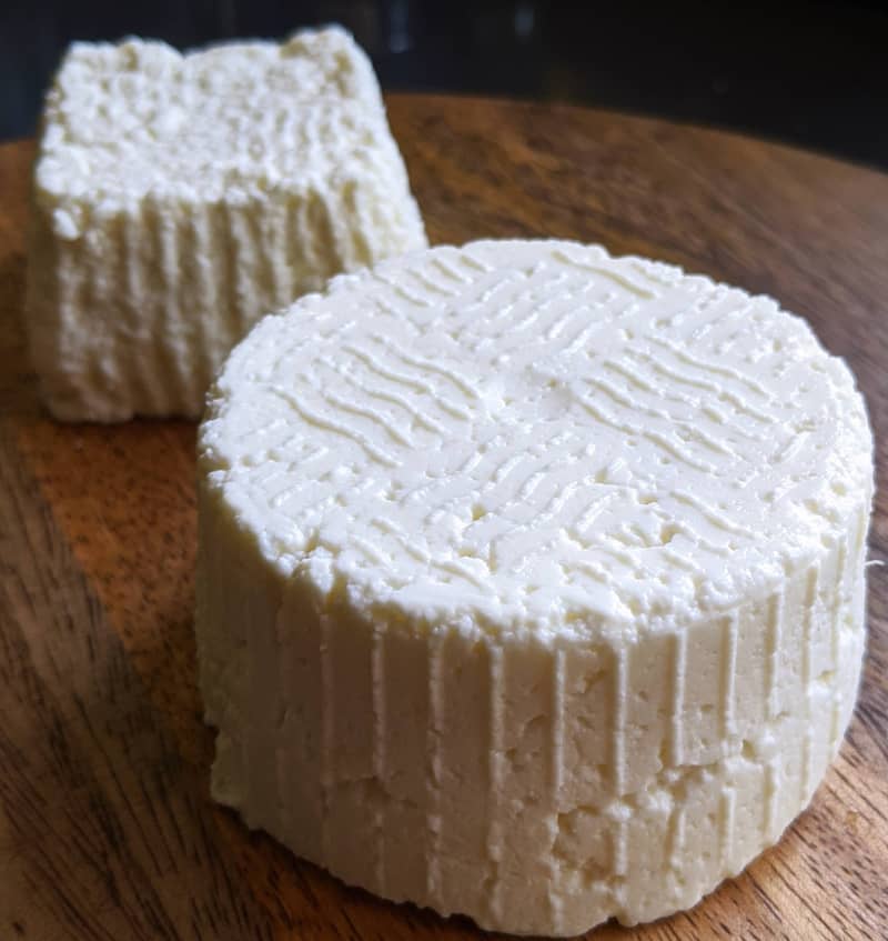 two wheels of fresh cheese on wood board