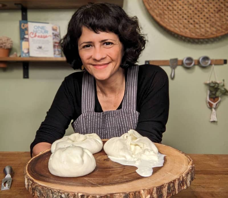 woman holding large wooden cheese platter with three large burrata cheeses