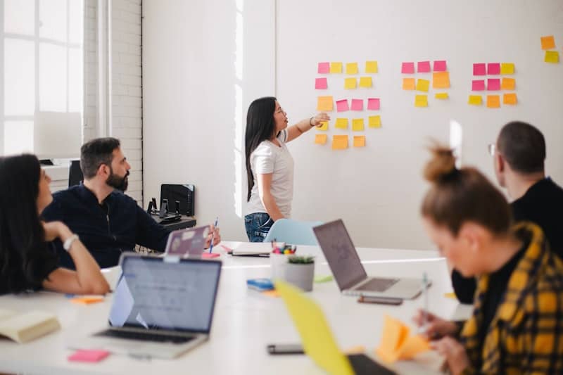 People sitting at a table looking at someone point at sticky notes on a board