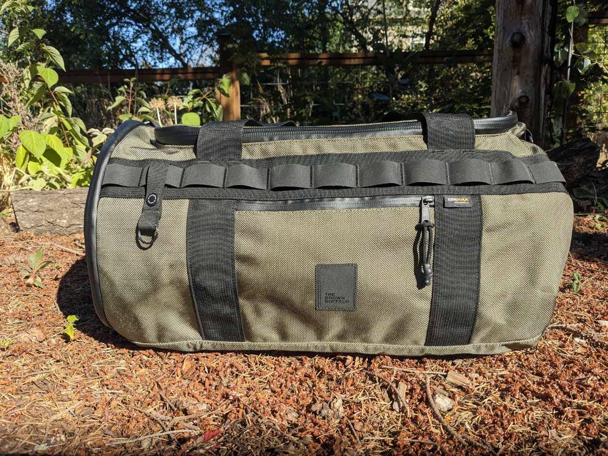 A brown Duffalo, a duffel bag for travel, on a pine needle covered trail.
