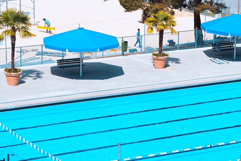 A blue pool with palm trees and umbrellas.