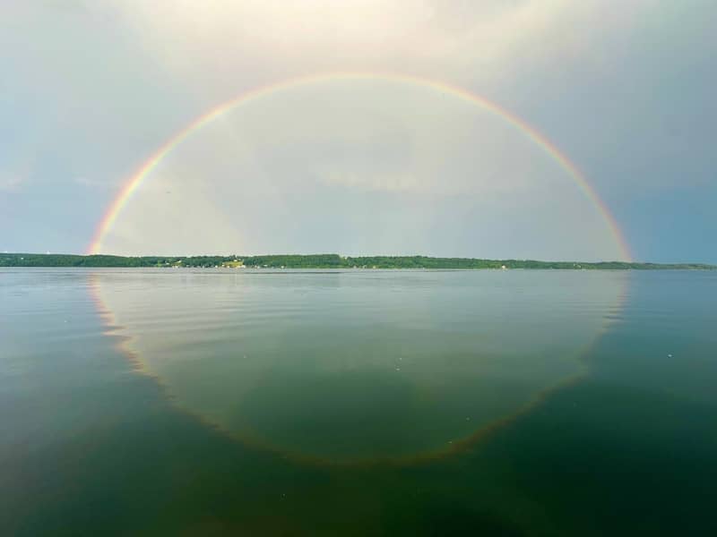 A complete rainbow arches over calm water.