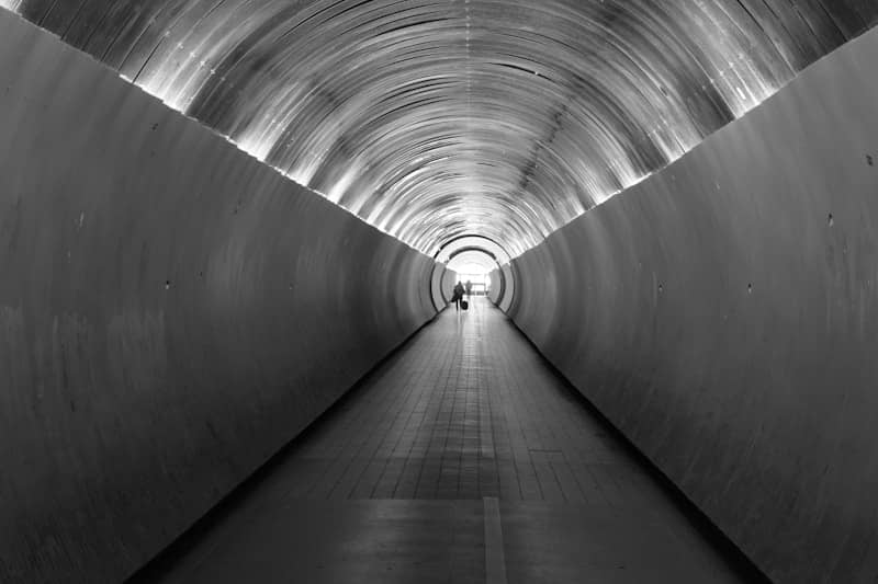 A person walks down a long, illuminated, circular tunnel.