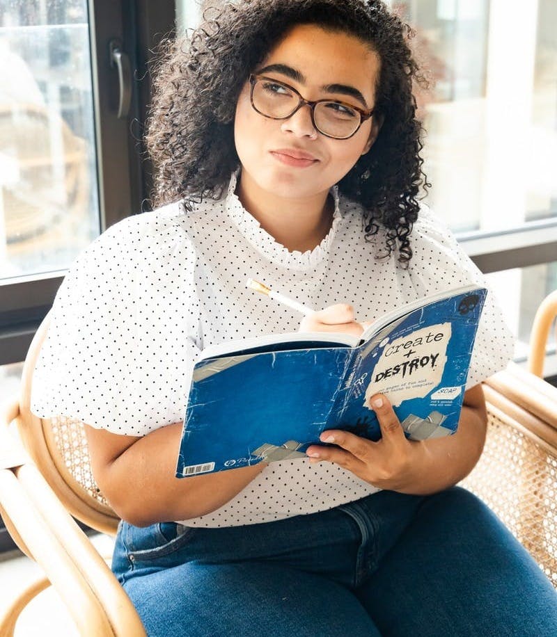 woman in white and black polka dot shirt holding blue and white book