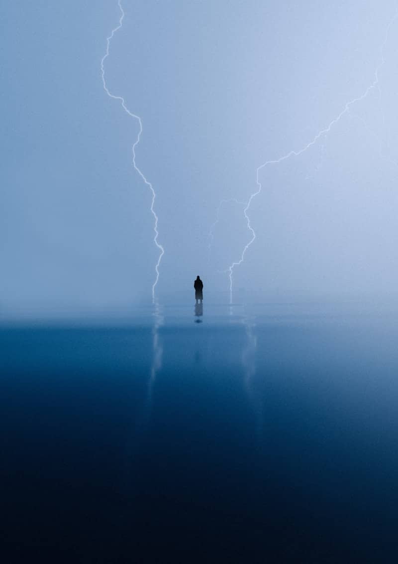 Una persona en medio de una masa de agua y rayos al fondo