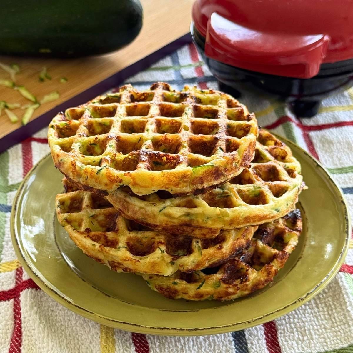 Four zucchini chaffles stacked on a green plate.