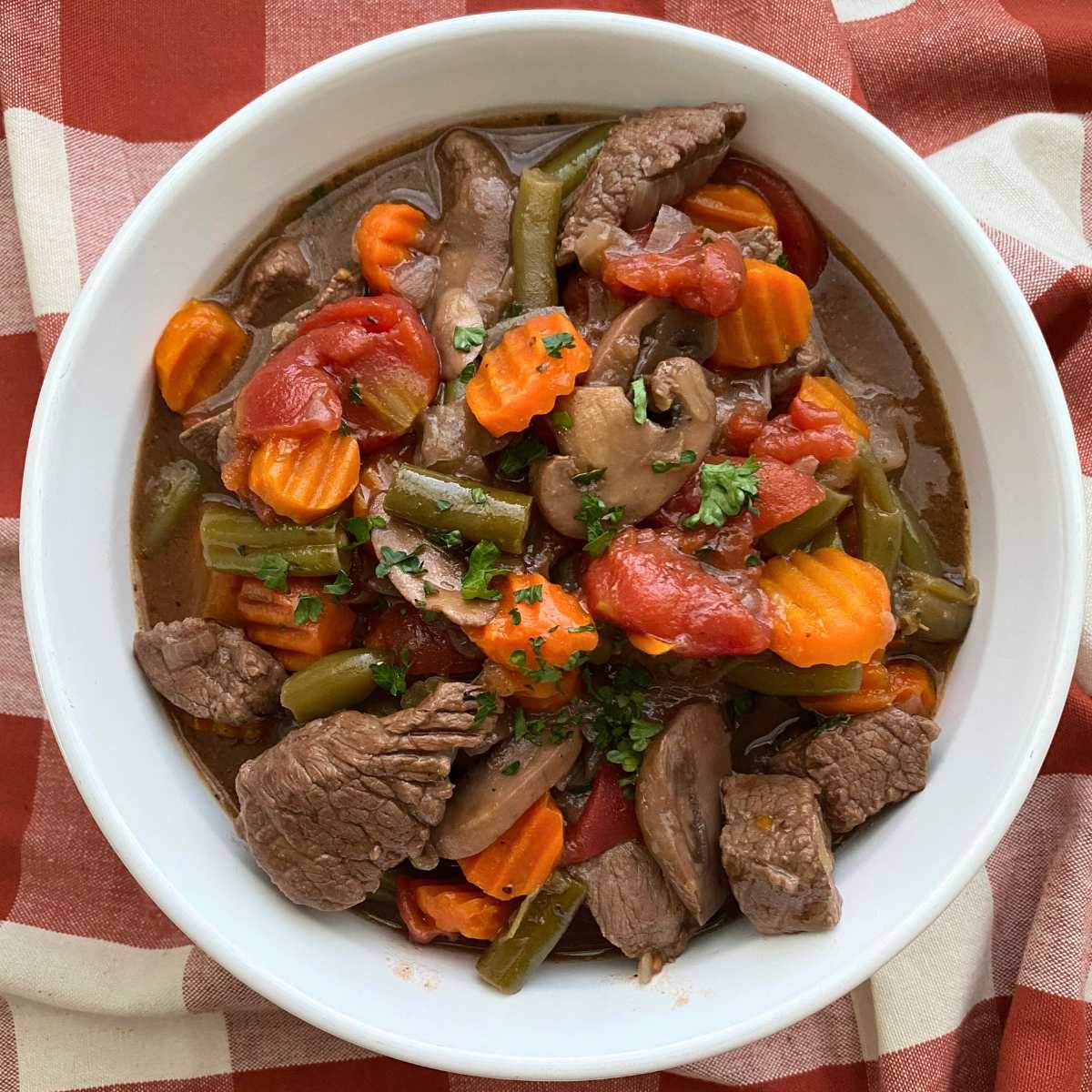 White bowl with beef stew and vegetables in a red wine sauce.