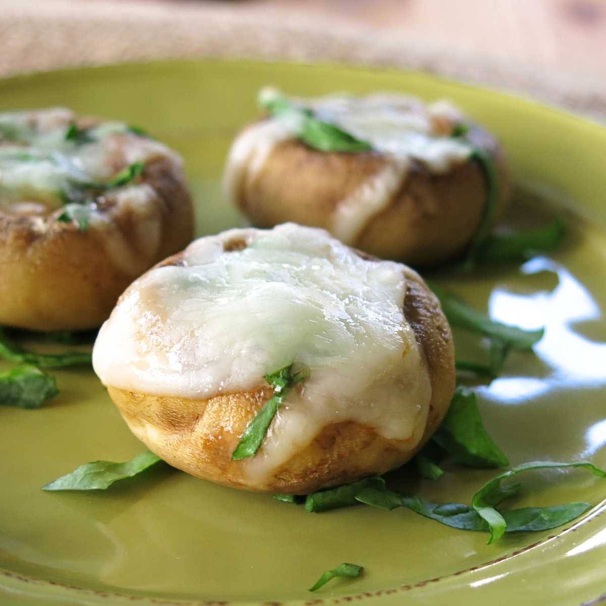 Mushroom cap pizza bites on a green plate.