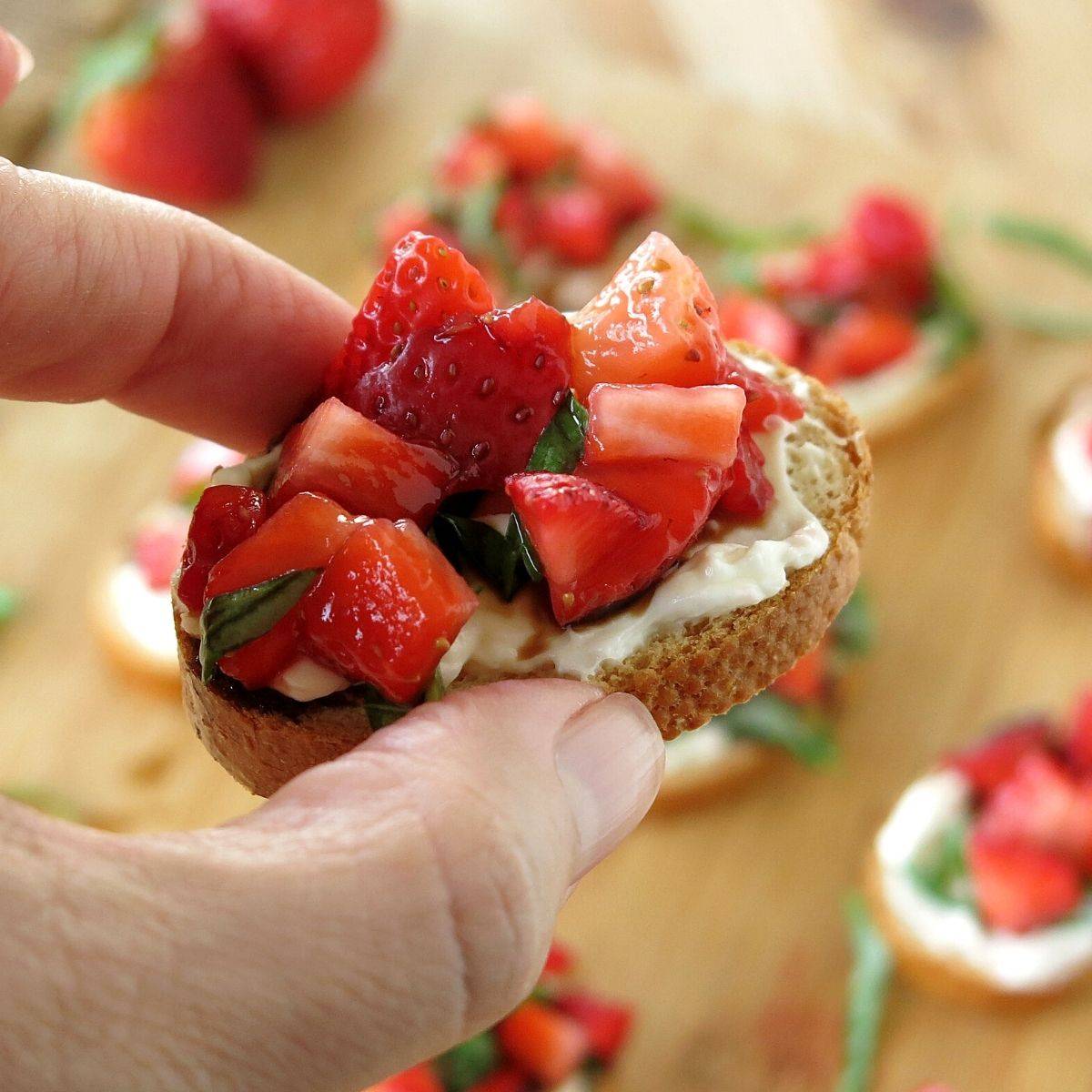 Fingers holding strawberry bruschetta.
