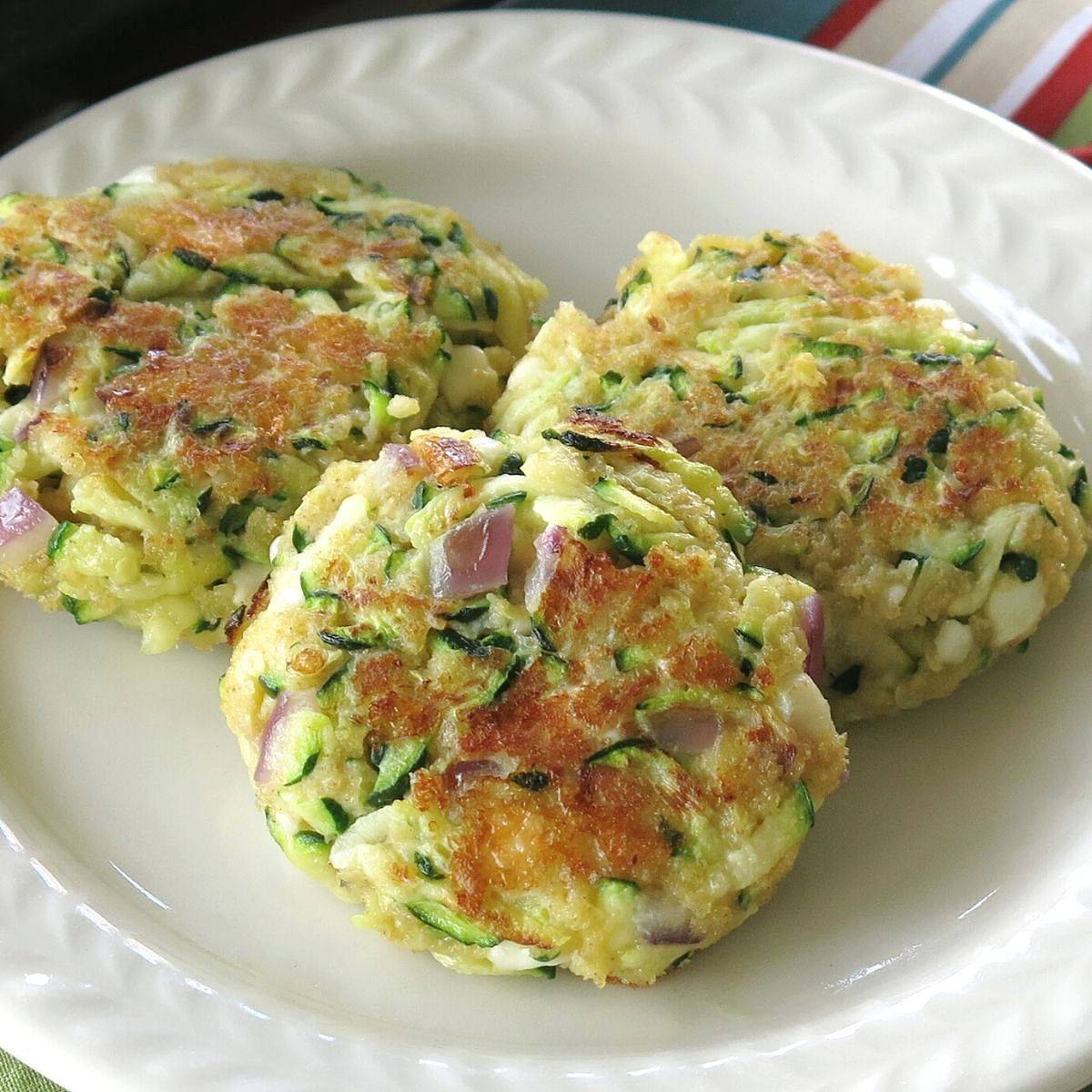Three fried zucchini cakes on a white plate.