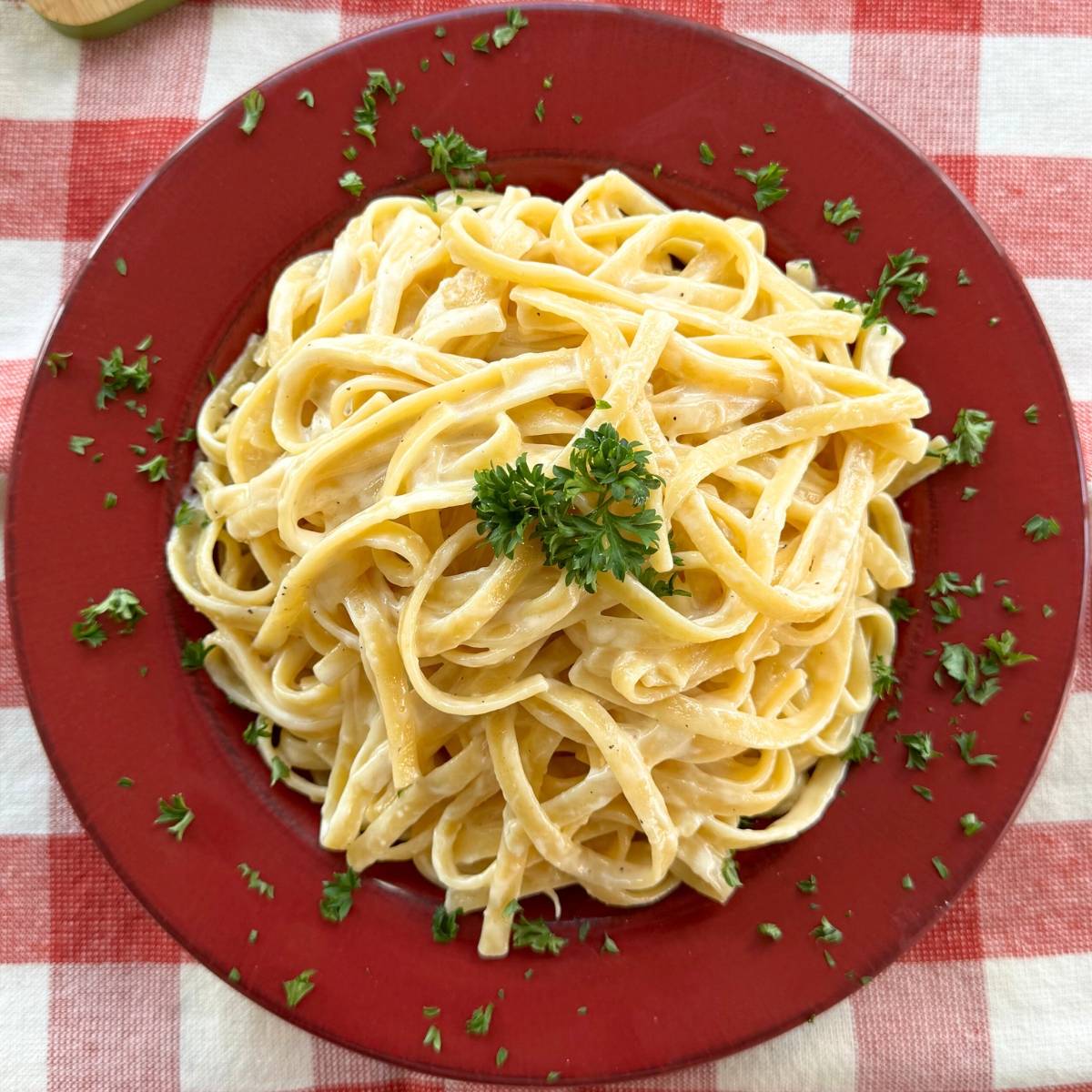 Fettuccine alfredo garnished with parsley in a red bowl.
