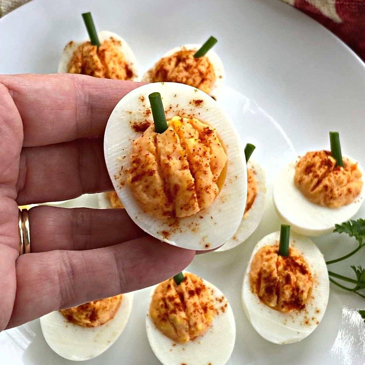Hand holding a pumpkin deviled egg over a plate with more on it.