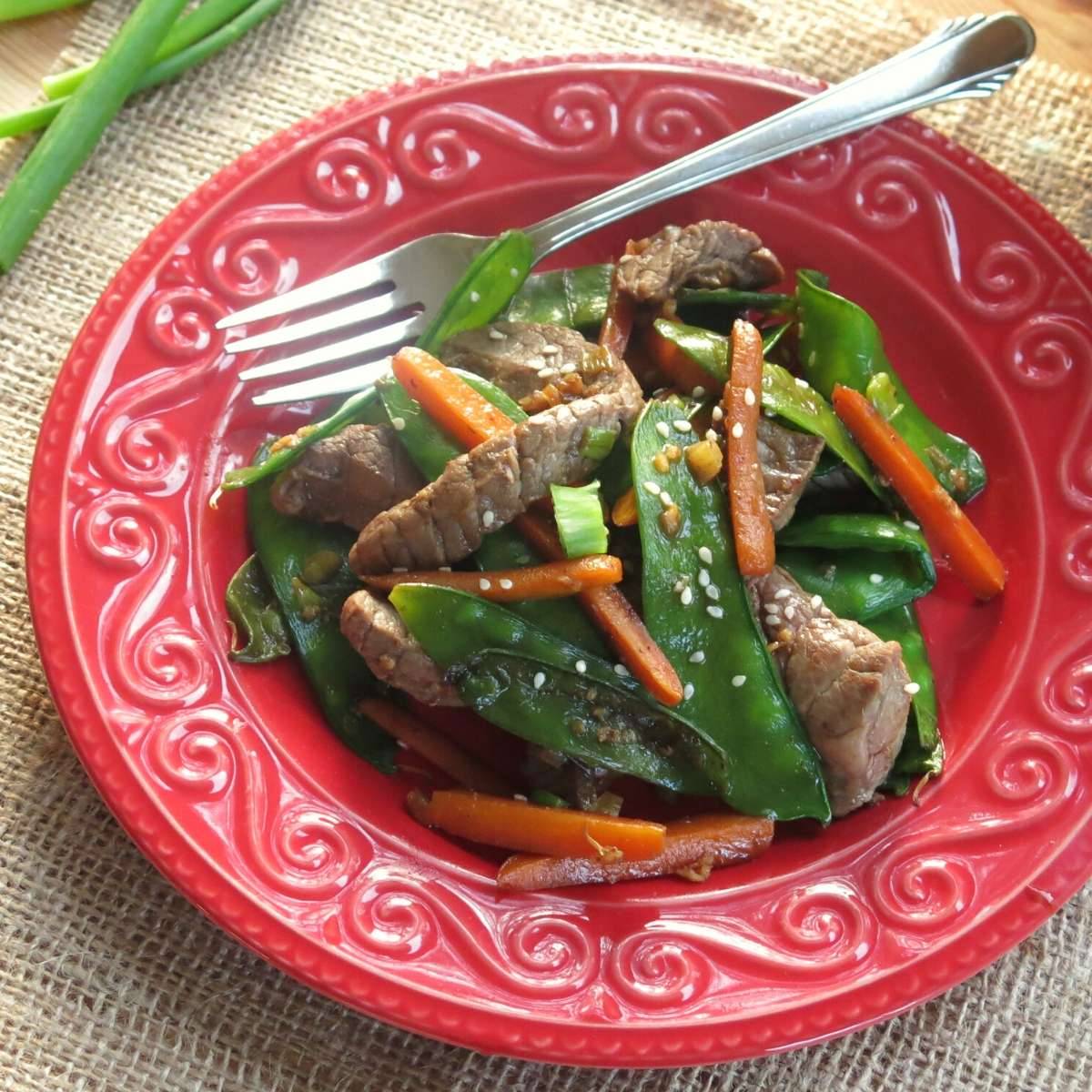 Sesame beef stir fry on a red plate with a fork.