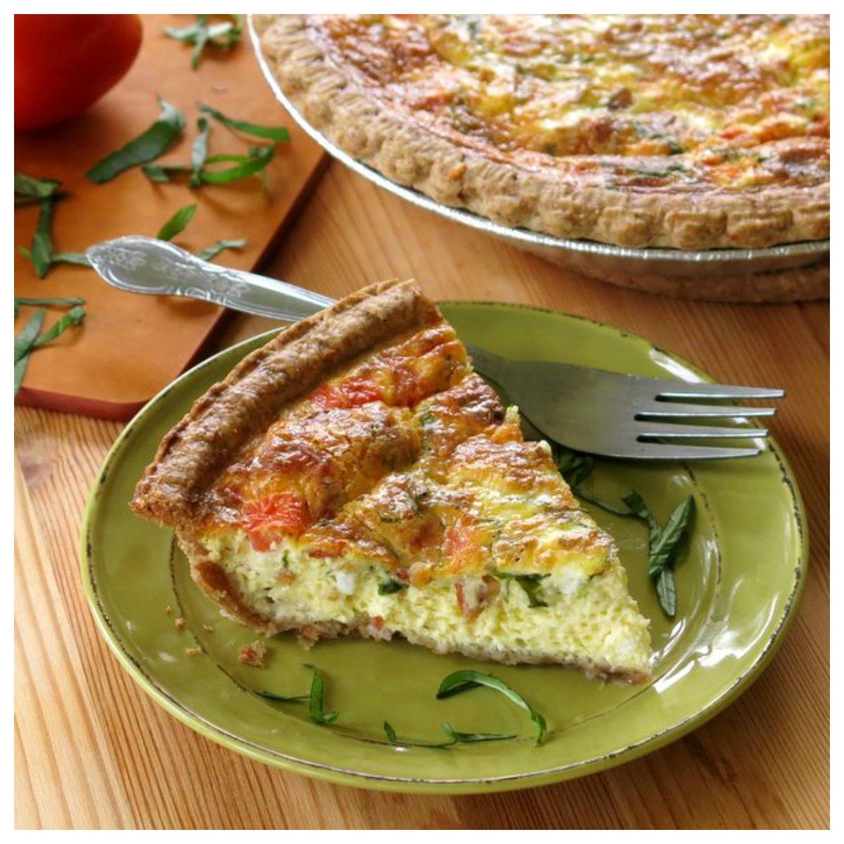 Tomato bacon quiche with fresh basil on a green plate with a fork.