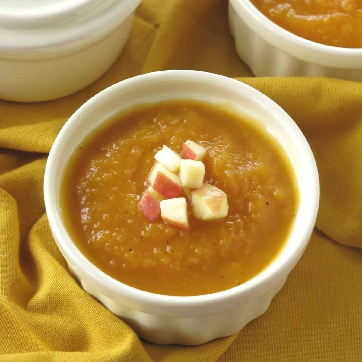 Butternut squash apple soup garnished with chopped apple on top in a cream bowl.