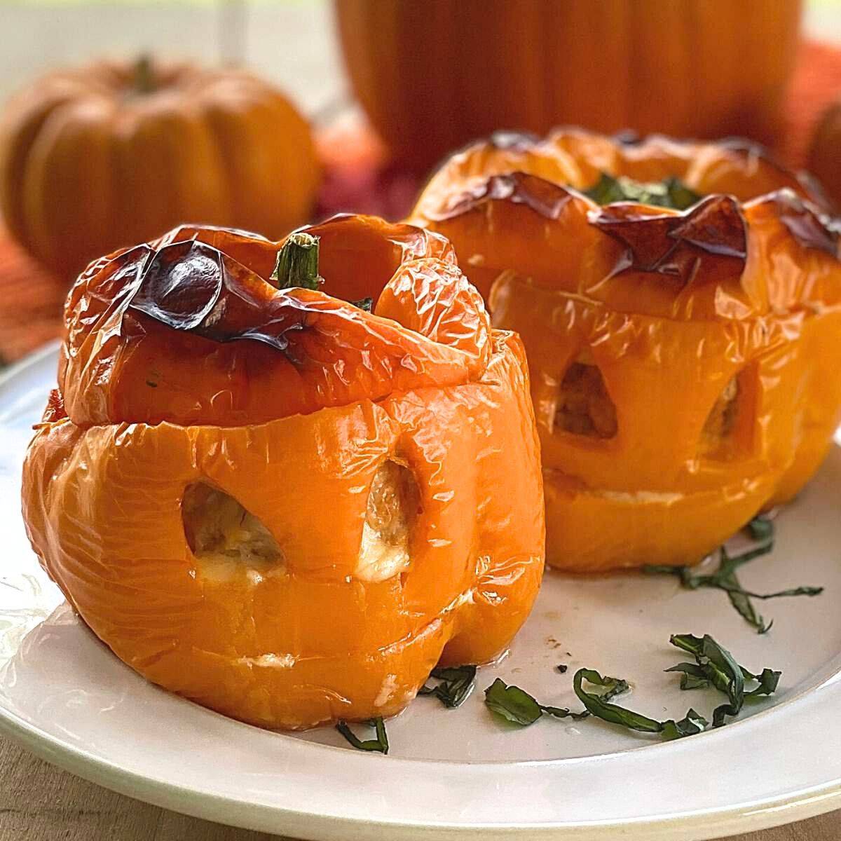 Two orange stuffed jack-o'-latern peppers on a plate.