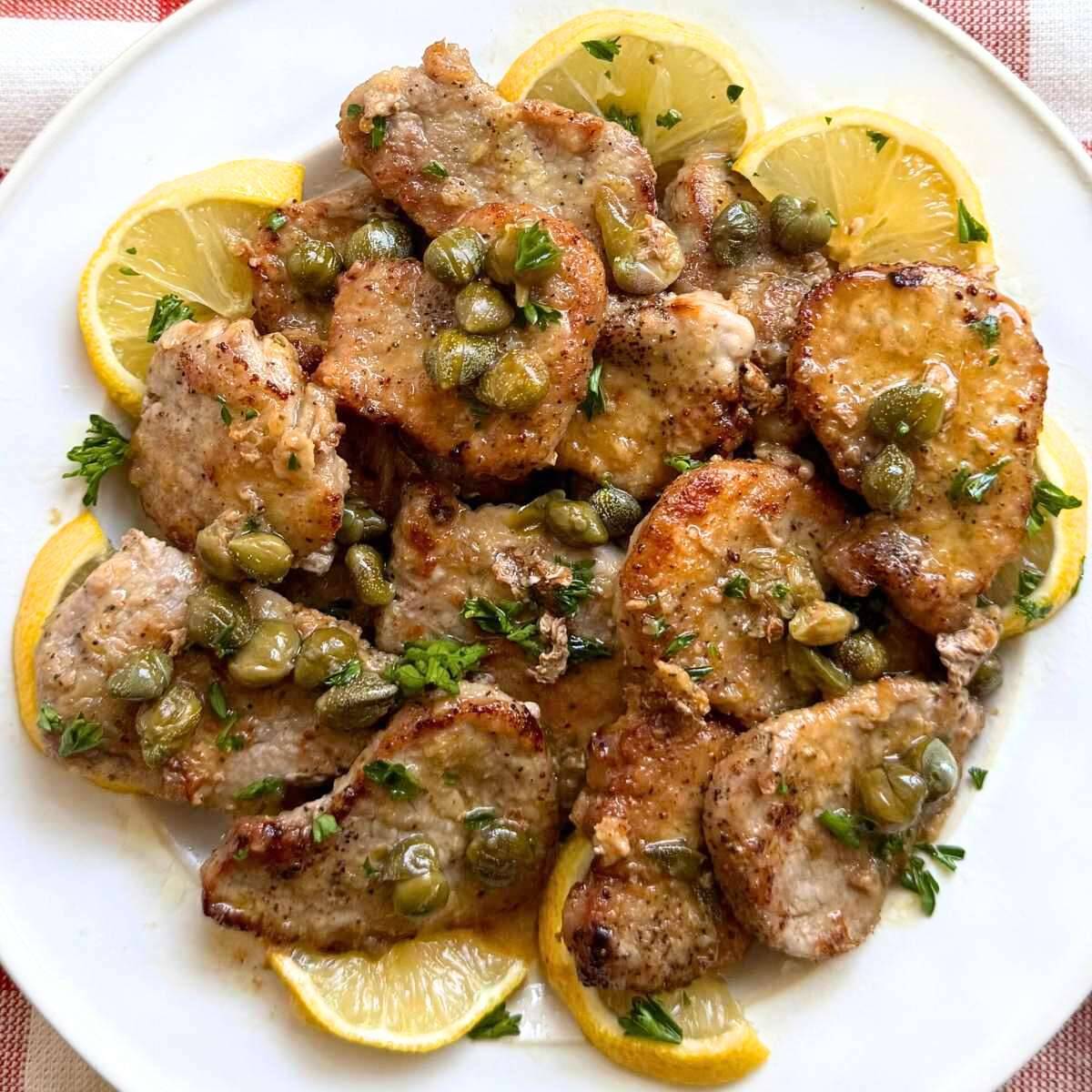 Pork Piccata on a white plate surrounded by lemon slices.