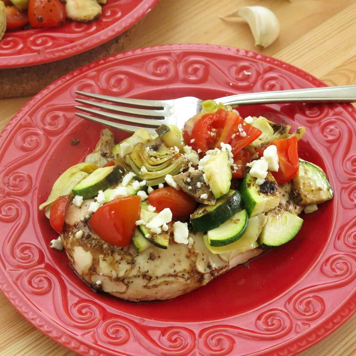 Mediterranean chicken on a red plate with a fork.