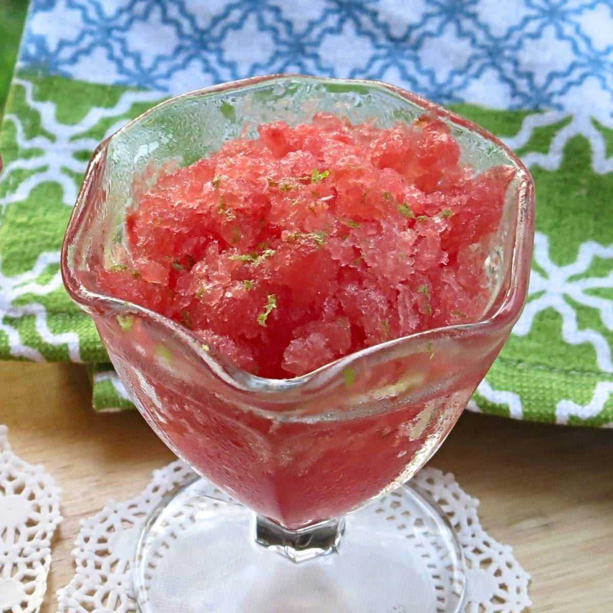 Glass dish holding watermelon granita with a colorful napkin in the background.