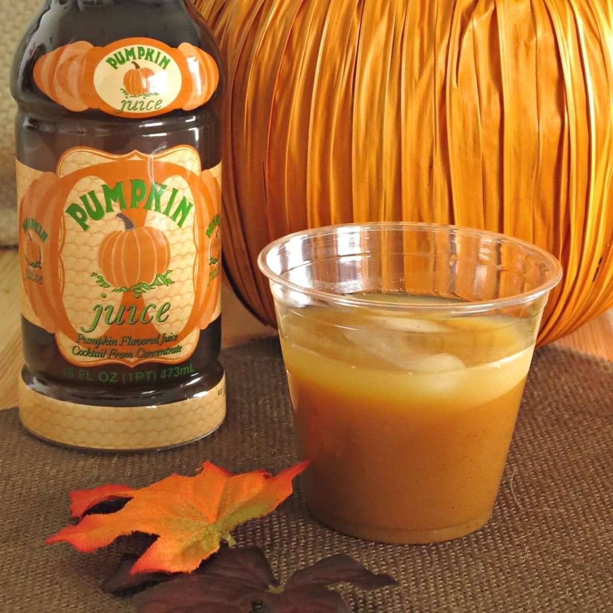 Pumpkin juice in a glass with a Harry-Potter bottle and pumpkin behind in.