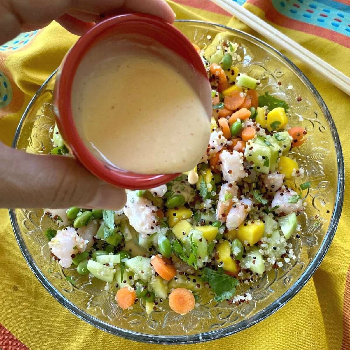 Creamy dressing being poured over a shrimp poke bowl.