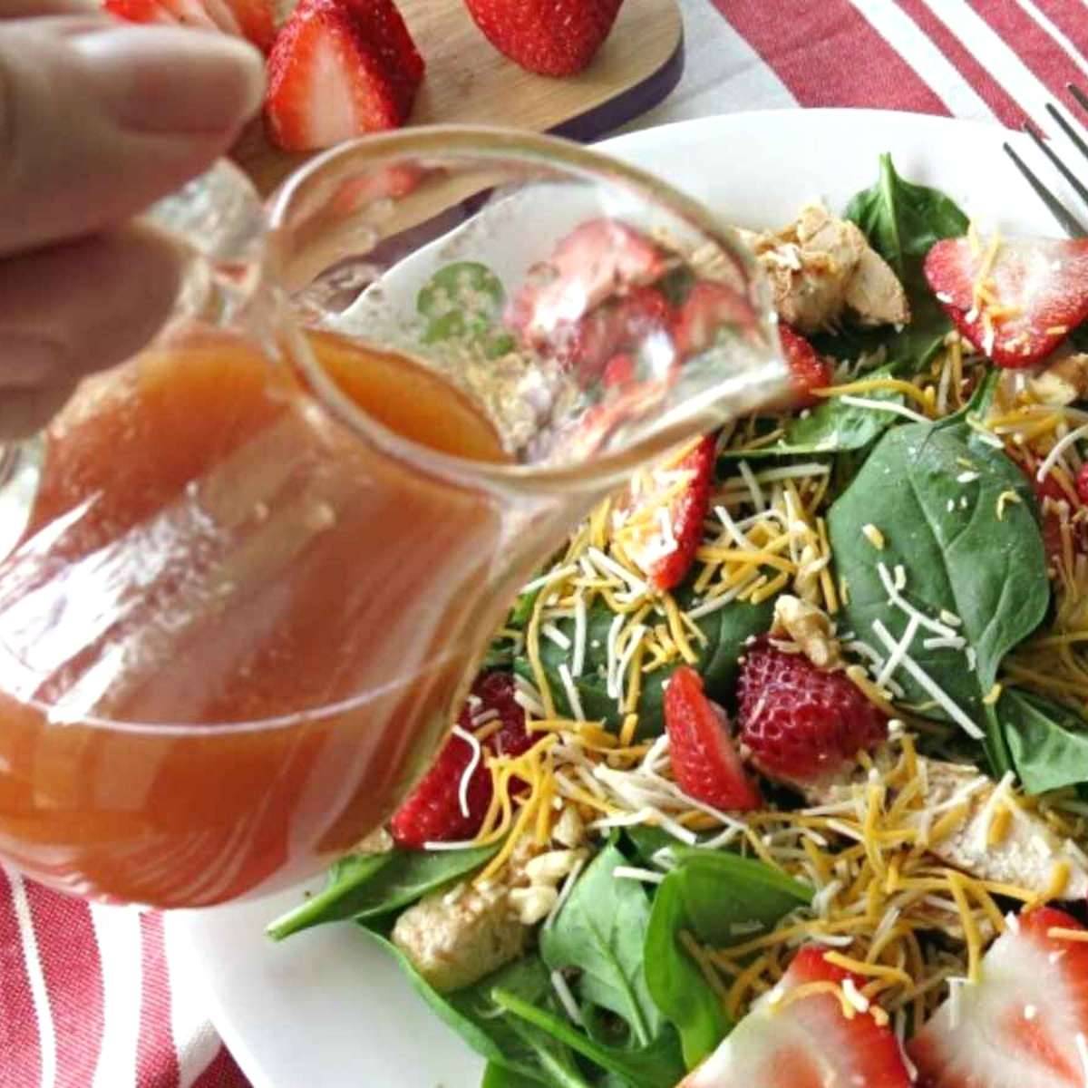 Sweet red wine vinaigrette dressing being poured over greens and strawberries.