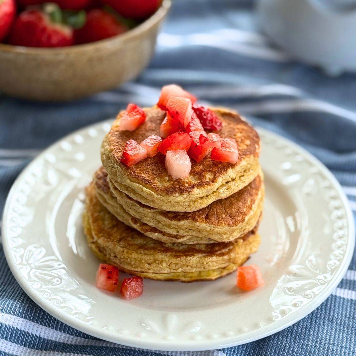 Stack of cottage cheese oat pancakes topped with diced strawberries on a white plate.