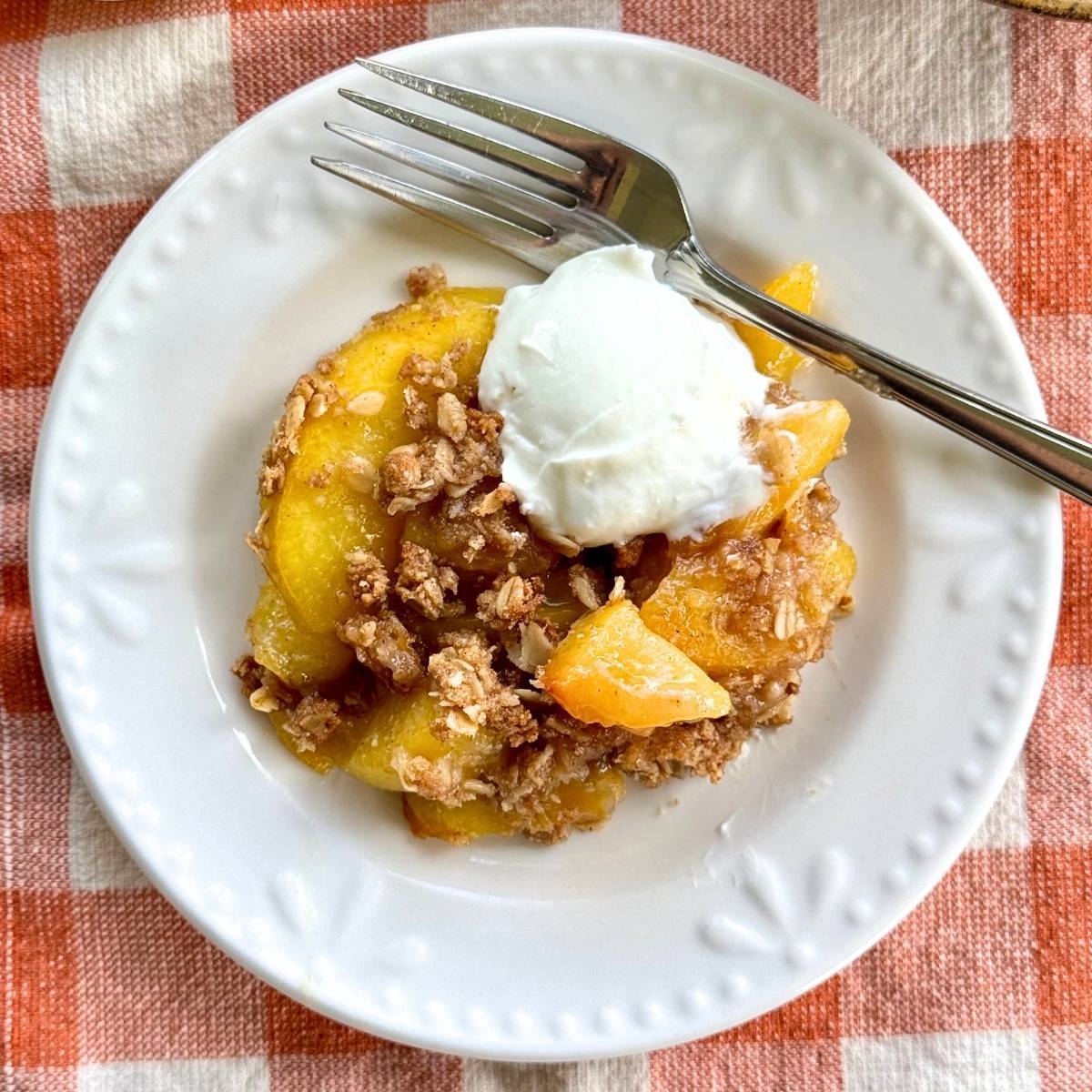 Peach crisp with oat and almond flour topping on a white plate.