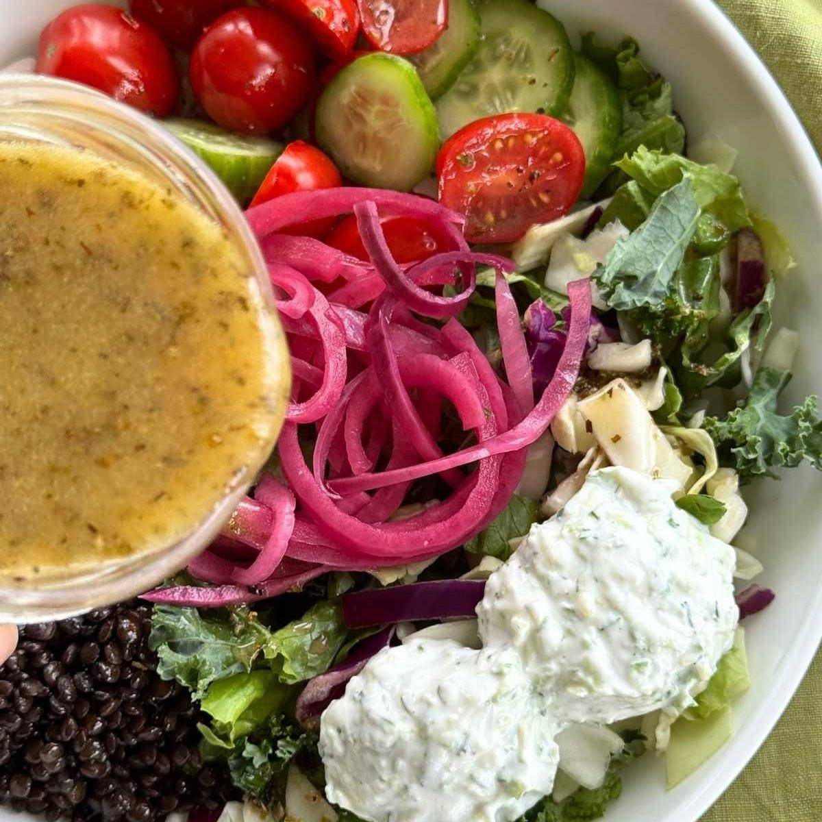 Greek vinaigrette being poured over Cava-inspired Mediterranean bowl.