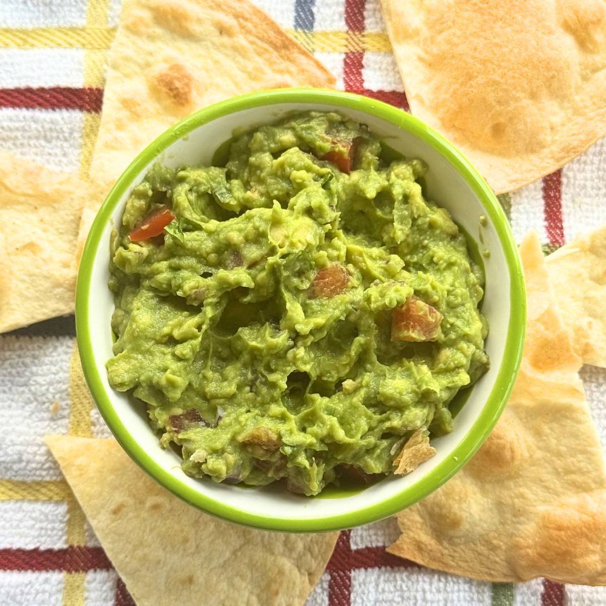One avocado guacamole in a bowl surrounding by chips.