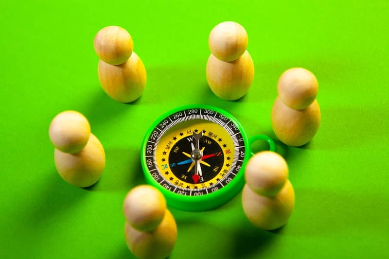 Wooden figures surround a green compass on a green surface
