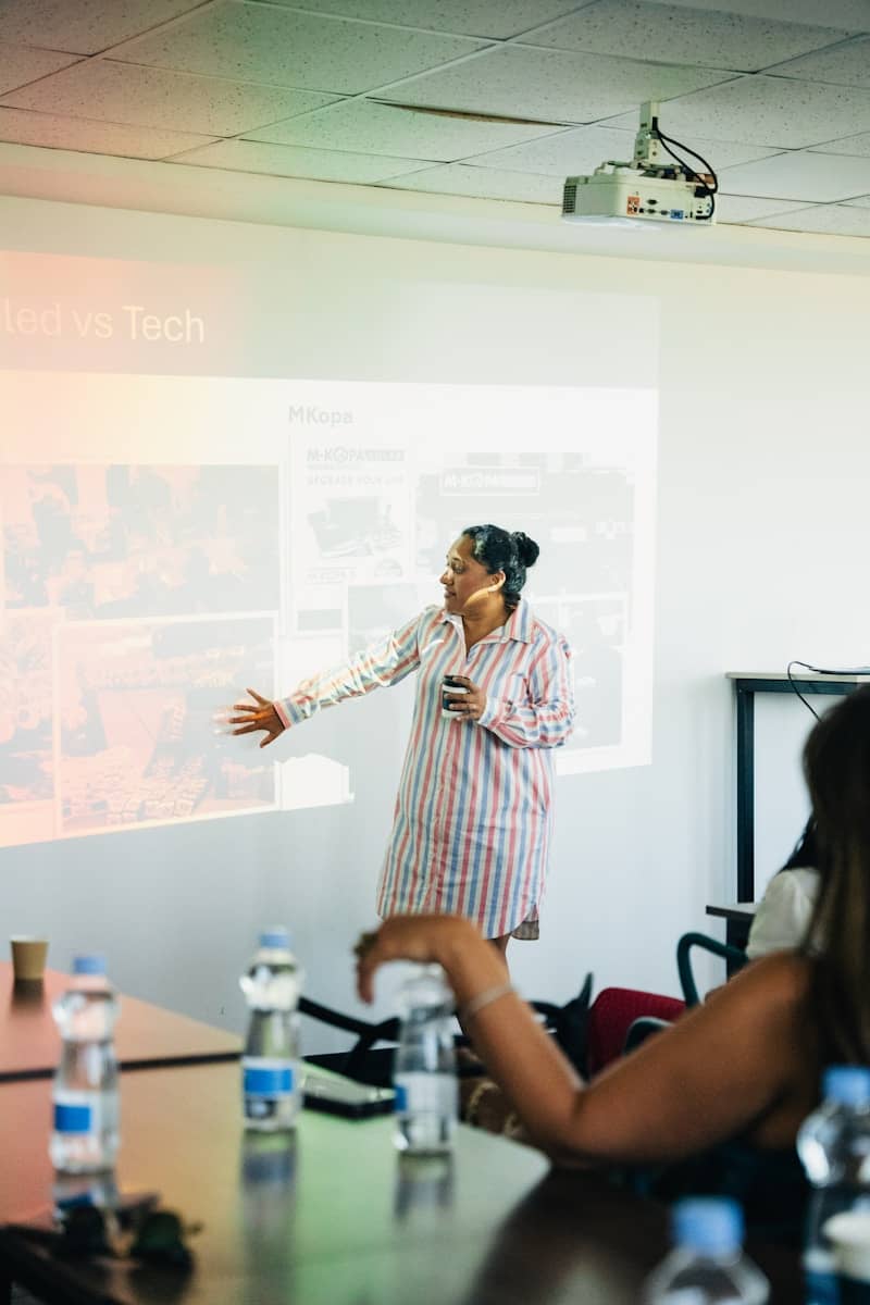 Woman presenting to audience near projector screen.
